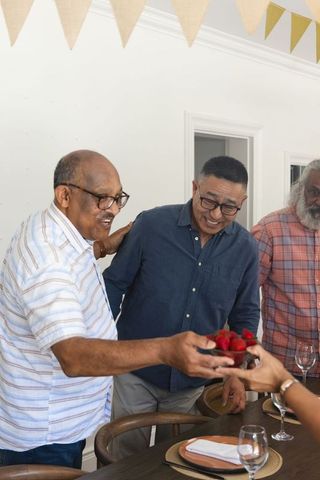 Multicultural senior men sharing strawberries around festive dining table