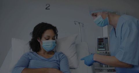 Nurse consulting masked patient at bedside in hospital ward monitoring iv pump