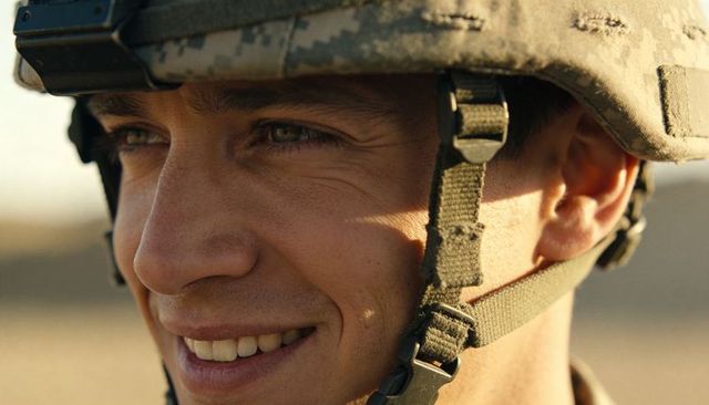 Smiling soldier wearing camouflage helmet and chin strap facing sunlit desert close-up