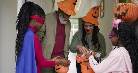 Family giving candy to african american trick-or-treaters wearing pumpkin hats at doorway