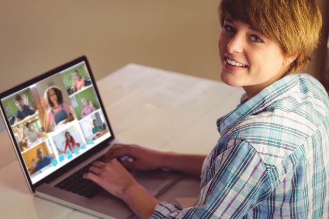 Young woman smiling while engaging in a video conference call on her laptop. Suitable for use in articles or advertisements related to remote work, online communication, telecommuting, online learning, digital technology, and home office environments.