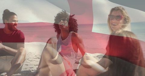 Laughing friends relaxing on sunny beach with translucent flag overlay, summer gathering