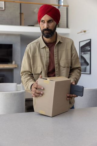 Man in Red Turban Holds Box and Uses Smartphone in Modern Kitchen