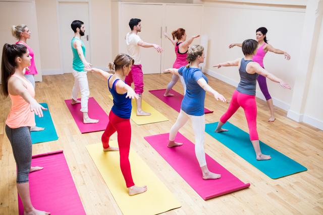 Group of people practicing yoga with an instructor in a fitness studio. Participants are stretching on colorful mats, focusing on balance and flexibility. Ideal for promoting group fitness classes, wellness programs, and healthy lifestyle activities.