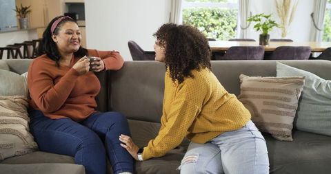 Mother and daughter sharing cozy conversation on gray sofa in knit sweaters holding mug