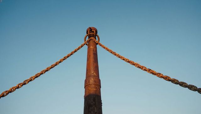Rusted mooring bollard displaying twisted chains against clear sky