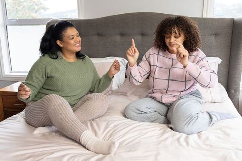 Diverse women chatting and laughing on cozy king bed in loungewear, casual home bedroom