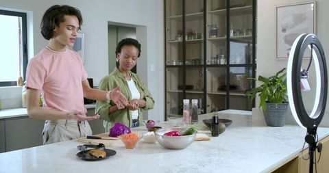 Diverse cohosts presenting live cooking tutorial on modern kitchen island with ring light