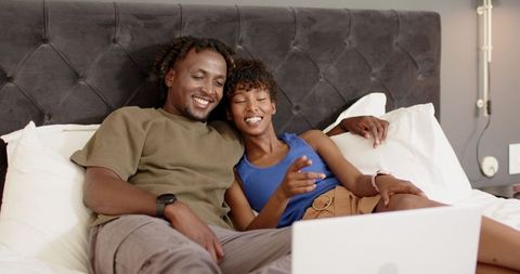 African couple relaxing on bed watching laptop, sharing cozy intimate moment at home