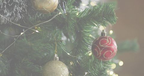 Red christmas bauble hanging on pine branch with warm bokeh lights and gold ornaments