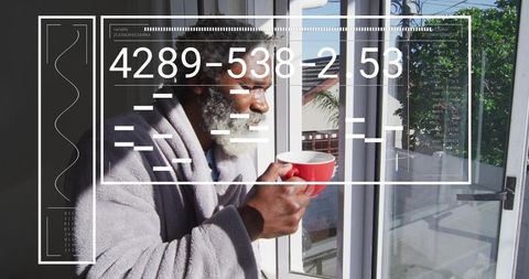Senior man holding red mug, sipping in gray bathrobe, looking out balcony with hud overlay