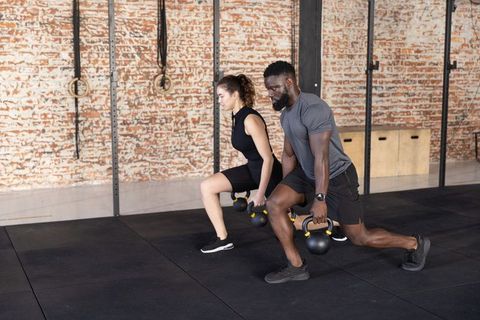 Diverse athletes performing kettlebell lunges in urban brick gym for functional strength