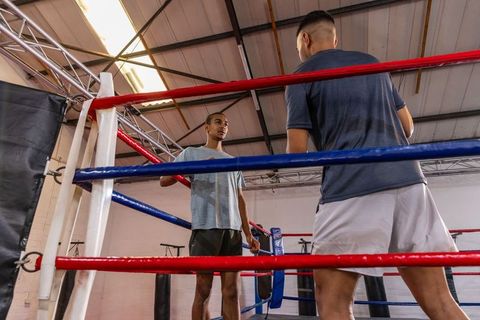 African american coach training young boxer in gritty warehouse boxing ring