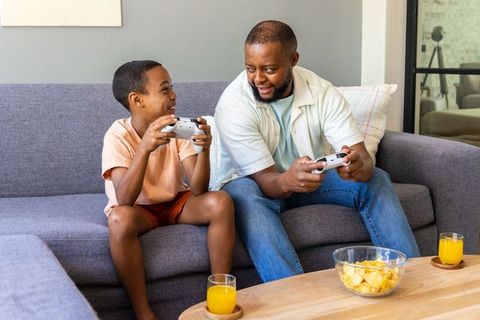 African american father and son playing video games on couch sharing snacks and laughter