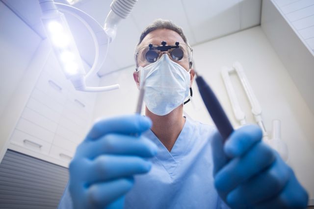 Dental assistant wearing gloves and mask, holding dental tools in a modern clinic. Ideal for use in healthcare, dentistry, and medical-related content. Suitable for illustrating dental care procedures, professional dental services, and hygiene practices in a clinical setting.