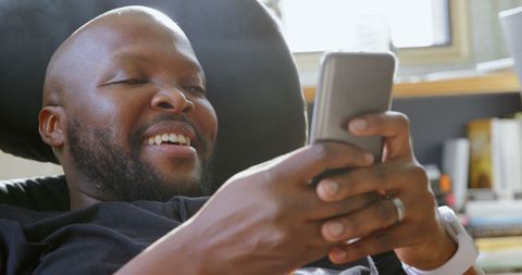 Smiling Man Relaxing at Home Using Smartphone