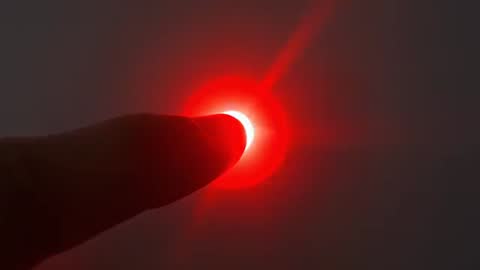 Finger pressing red LED on control panel creating glowing halo flare for touch feedback