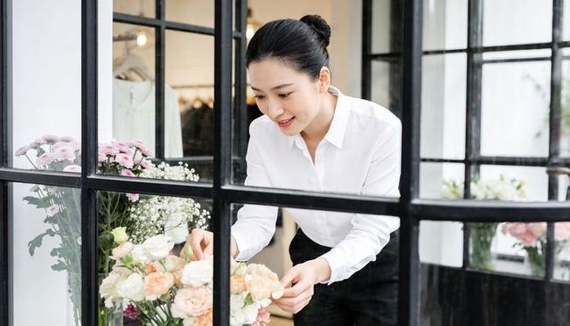 Floral boutique florist arranging pastel mixed bouquet behind black glass partition