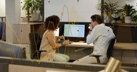 Collaborative team analyzing sales spreadsheet on dual monitors with financial chart overlay