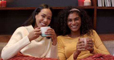 Diverse female friends relaxing with warm beverages on sofa