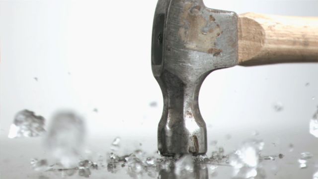 Dynamic close-up of hammer breaking ice cube in slow motion emphasizes impact and force. Useful for advertising tools, illustrating strength and destruction, or demonstrating slow-motion effects.