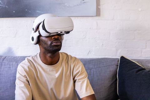 African man wearing white vr headset sitting on couch exploring immersive virtual reality