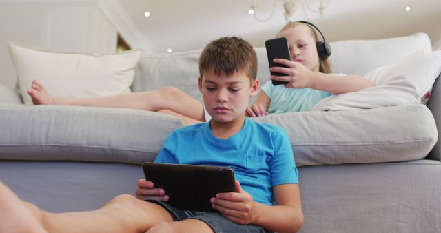 Portrait of caucasian brother and sister lying on sofa using tablet and smartphone - Download Free Stock Photos Pikwizard.com