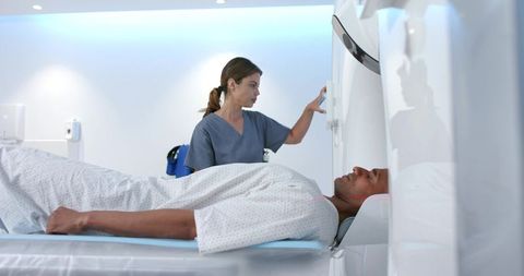 African american radiologic technologist adjusting ct gantry, male patient lying supine