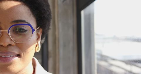 Confident Woman in Blue Glasses by Sunlit Office Window