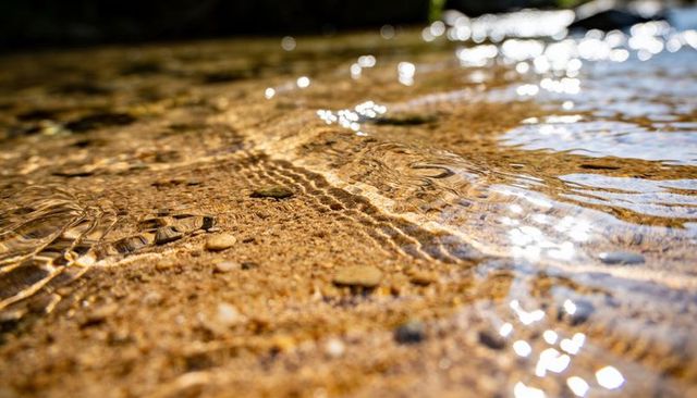 Sunlight shimmering on rippling shallow riverbed revealing sand and pebbles