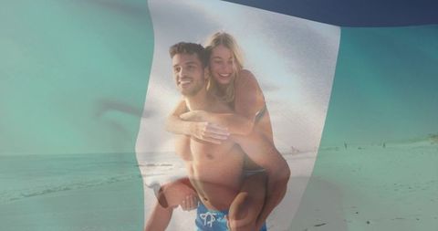Hispanic man carrying partner piggyback on beach with translucent green flag overlay