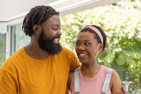 Smiling young couple sharing warm moment by sliding glass door with sunlit backyard