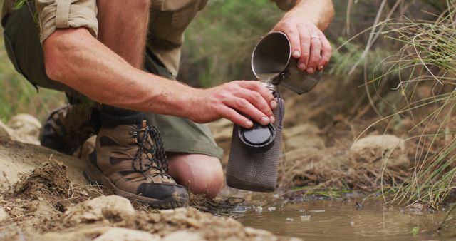 Caucasian male survivalist scooping water from stream and pouring into drinking filter bottle. exploration, travel and adventure, survivalist in nature.
