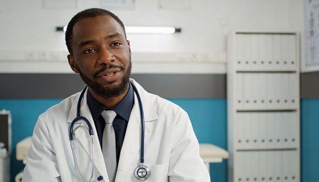 Male physician speaking with patient in clinic exam room wearing stethoscope and tie