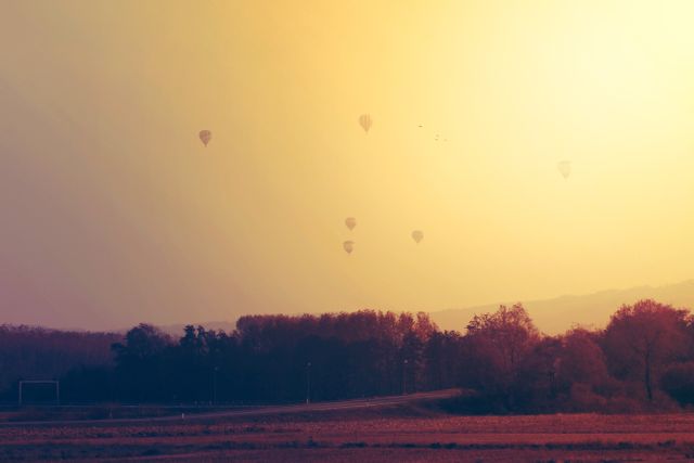 This tranquil scene features hot air balloons floating over the countryside at sunset with a view of the horizon and trees below. Perfect for travel and adventure promotions, inspirational posters, or serene landscape features, it evokes a sense of calm and exploration.