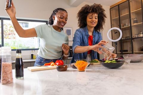 African american women recording cooking vlog preparing fresh salad in modern kitchen