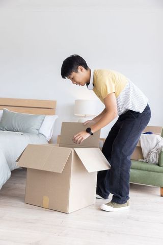 Young man unpacking moving box in bright minimalist bedroom during apartment move-in