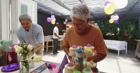 Senior woman arranging colorful cupcakes at multigenerational backyard birthday celebration