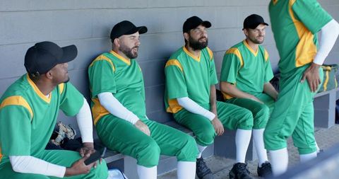 Baseball team relaxing in dugout wearing green and yellow uniforms during game break
