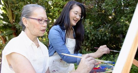 Multigenerational asian women painting together in sunny backyard garden with palette