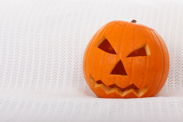 A carved pumpkin with a spooky face used as Halloween decor sits on a couch with a white background. Perfect for Halloween-themed promotions, festive holiday designs, greeting cards, party invitations, and seasonal marketing materials.