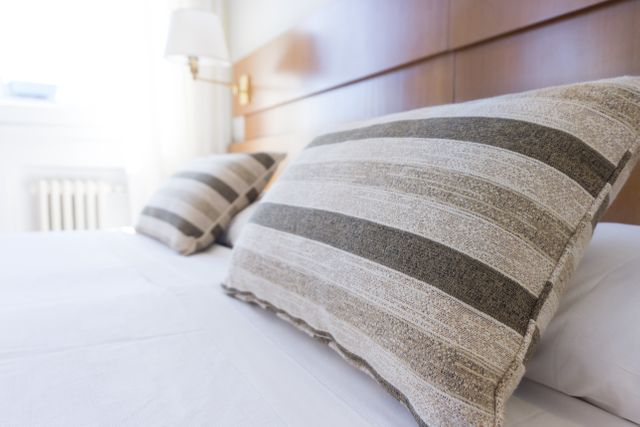 Perfect for illustrating bedroom interior design, promoting relaxation or hospitality contexts such as hotels or guesthouses. The soft sunlight and comfortable bedding evoke feelings of coziness and comfort, ideal for marketing home textiles or staging a serene living space.