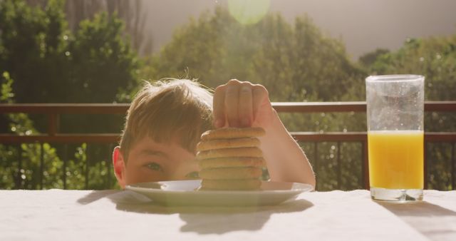 Child eagerly reaching for a stack of cookies on a sunny morning with a glass of orange juice beside. Ideal for themes related to childhood innocence, playfulness, food temptations, and happy summer memories. Perfect for use in family-oriented advertisements, parenting blogs, and children's storybooks.