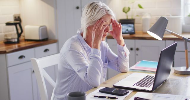 Thoughtful senior caucasian woman sitting at table in kitchen, using laptop - Download Free Stock Photos Pikwizard.com