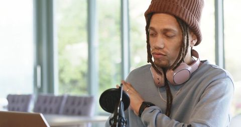 Mid-adult man podcasting with headphones and microphone near bright window and laptop