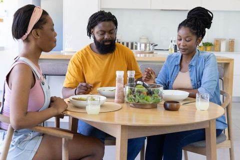 African family sharing healthy salad around sunlit round wooden table in modern kitchen
