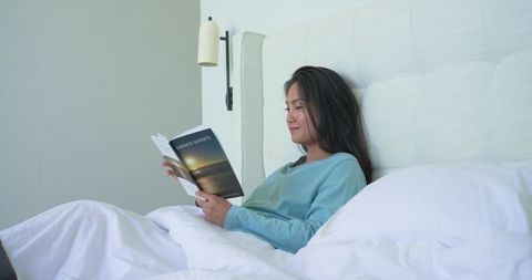 Mid-adult asian woman reading in bed | serene minimalist bedroom scene for relaxation