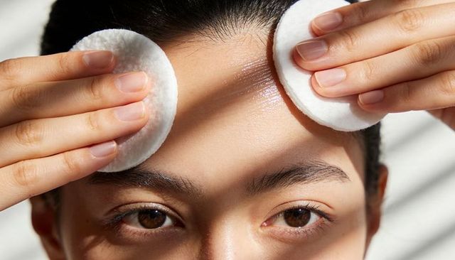 Asian woman pressing cotton pads on forehead for gentle morning skincare routine
