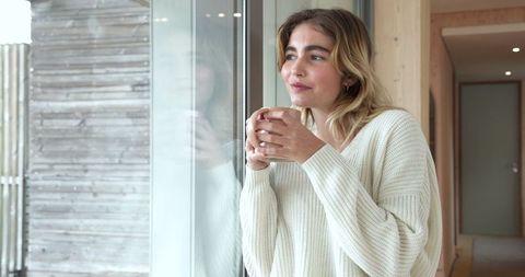 Thoughtful Woman Enjoying Warm Drink by Window in Modern Home Setting