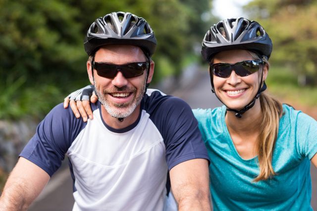 Smiling athletic couple wearing helmets while riding bicycle